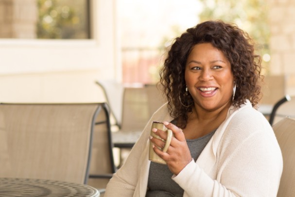 A woman smiles while sipping a hot beverage from a mug.