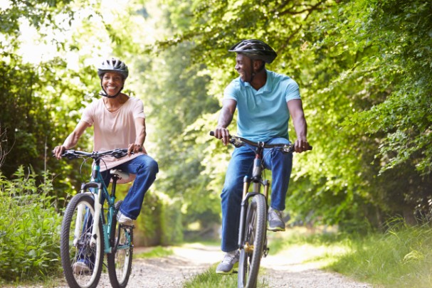 An older couple bike down a path in a wooded area 