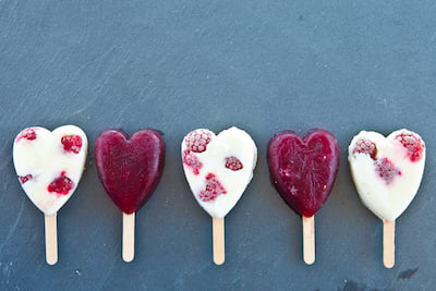 Berry popsicles in the shape of hearts lay in a line. 