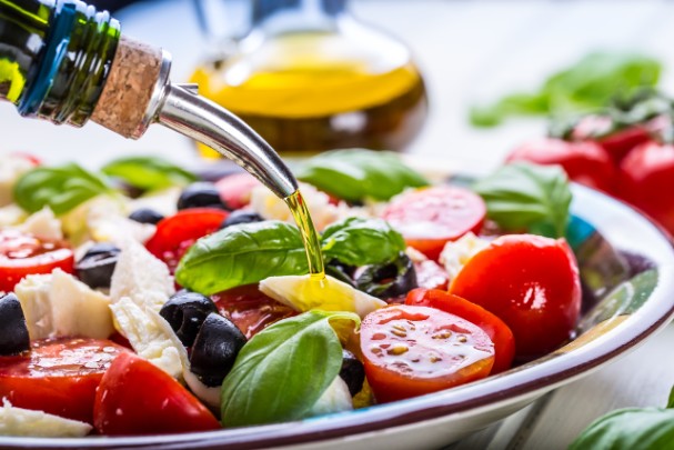 A person drizzles olive oil over a Mediterranean salad 