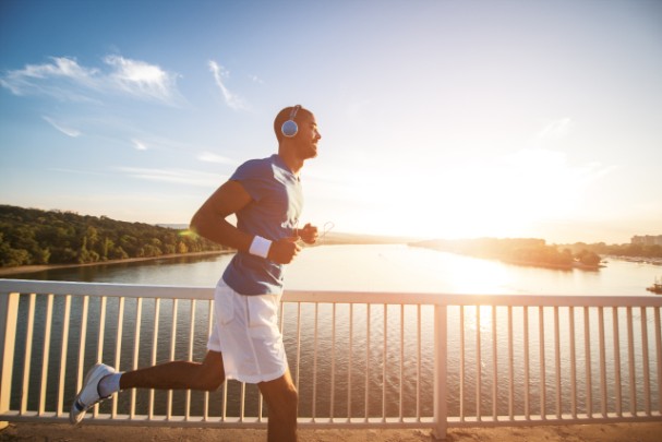 A man runs across by a lake with a sunset in the background