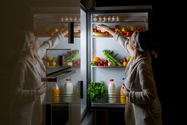 A woman reaches into her fridge for a late-night snack. 