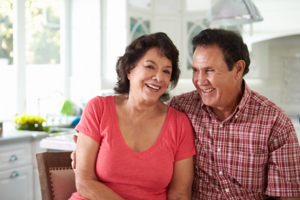 An older couple happily sit together in a kitchen 