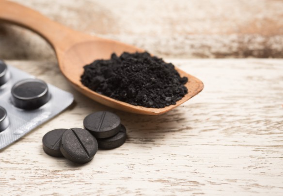 A spoonful of activated charcoal powder sits next to an activated charcoal tab