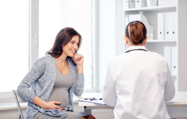 A pregnant woman sits and speaks with her doctor 