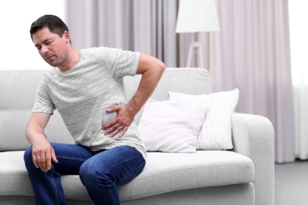 A man sits on a couch and clutches his side in pain 