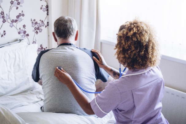 A doctor listens to an older man's breathing with a stethoscope