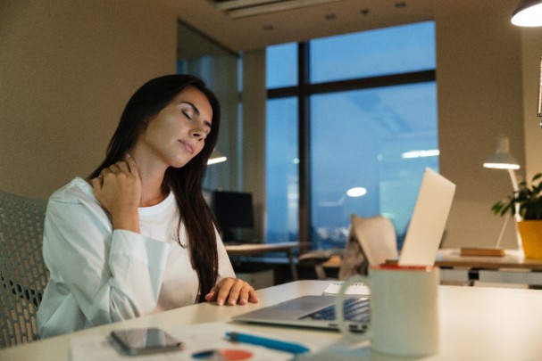 Woman rubs her aching neck as she sits at a computer