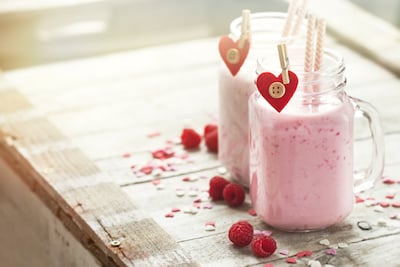 Two pink smoothies in mason jars sit on a table.  