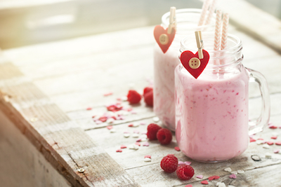 Two pink smoothies in mason jars sit on a table. 