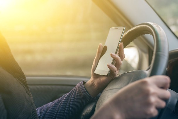 A person holds their phone up next to the steering wheel while driving