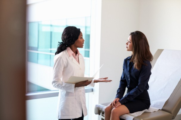 A doctor speaks with a woman sitting on a hospital bed 