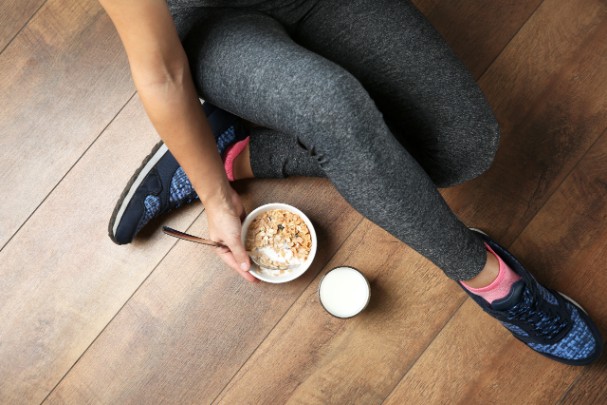 A woman sits on the floor and eats cereal 