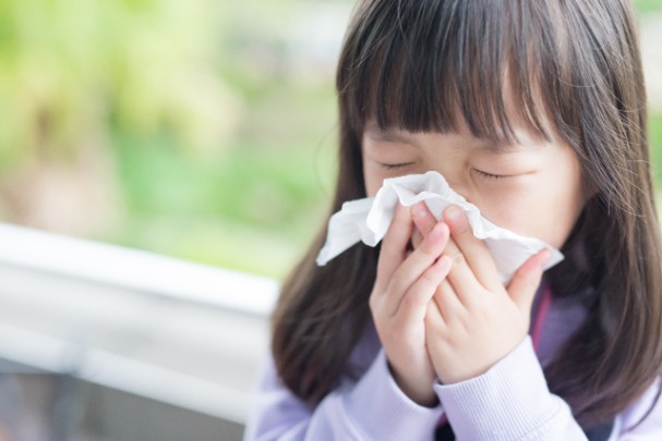 A young girl blows her nose into a tissue. 