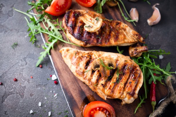 Grilled chicken breasts sit on a cutting board next to vegetables 