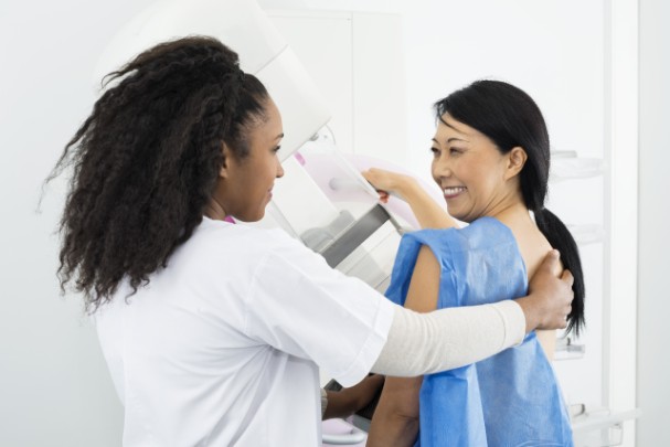 A mammography tech helps a woman get ready for her mammogram. 