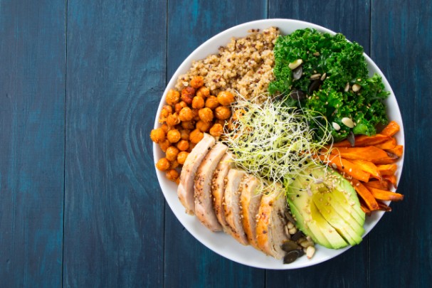 A bowl full of chicken, avocado, chickpeas, and other healthy ingredients sits on a counter
