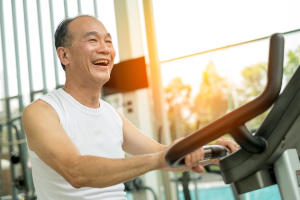 An older man happily exercises with a stationary bike. 