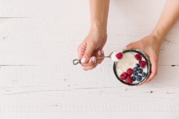 A woman eats a cup of yogurt and berries. 