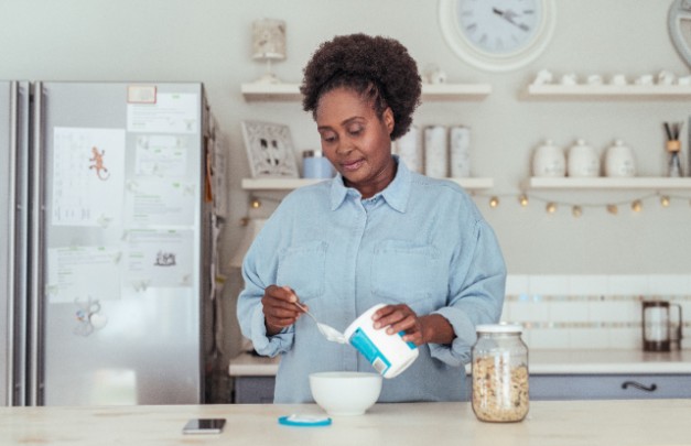 A woman spoons yogurt into a bowl. 