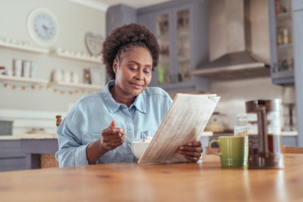 A woman reads a newspaper while eating breakfast at a table 