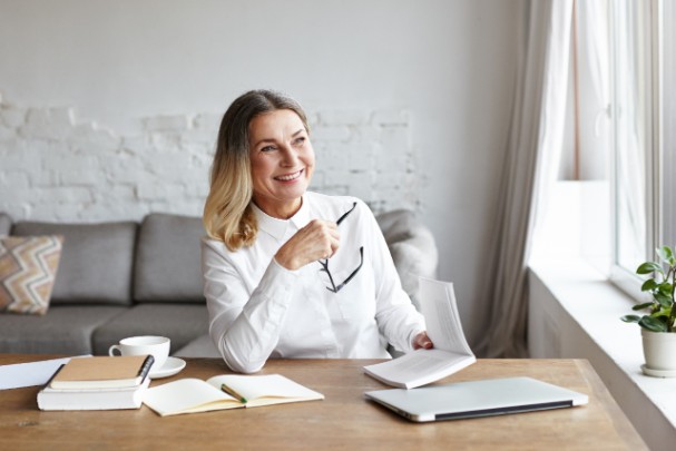 A woman smiles while looking off into the distance and holding her glasses in her hand.