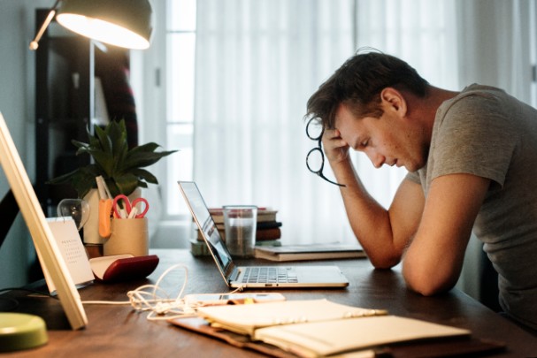 A man looks down at his laptop and rubs his forehead