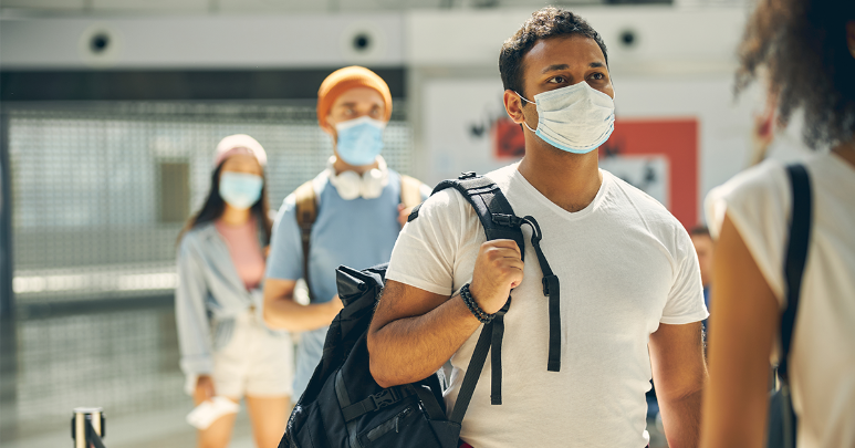 A young man stands in line at the airport while keeping COVID-19 safety tips in mind during travel.