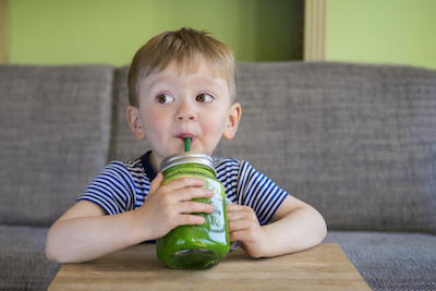 A toddler drinks a green smoothie.