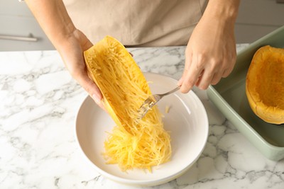 A person scrapes cooked spaghetti squash out of the skin.