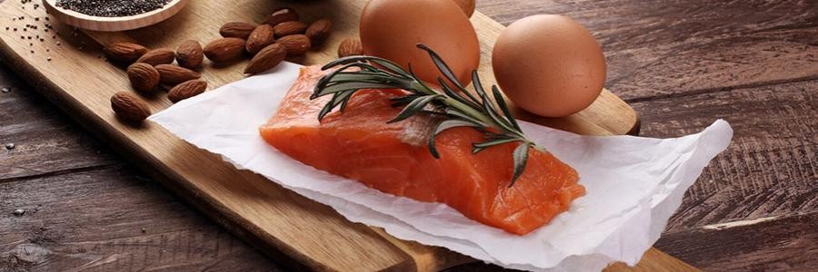 Piece of raw salmon, handful of almonds, and two eggs on a table