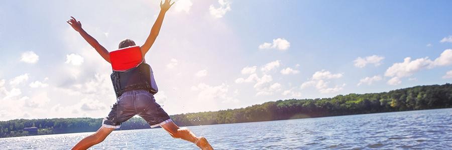 Boy jumping into lake wearing life vest