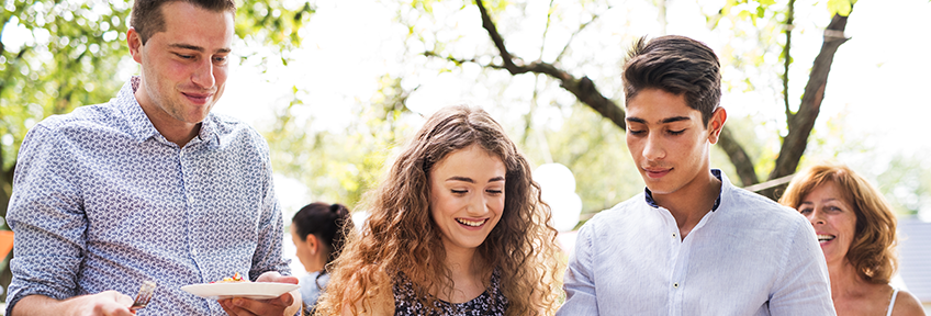 Young adults, fully vaccinated against COVID-19, pick up food from a buffet at a small outdoor gathering.