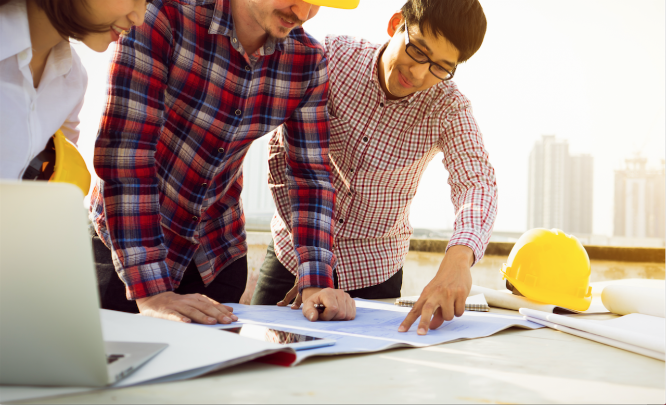 Three workers inspect blueprints on a job site